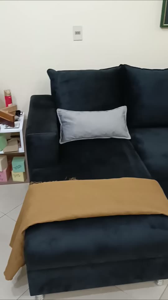 Sofá esquinero oscuro con almohadones grises, del video